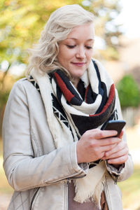 Mid adult woman holding phone while standing outdoors