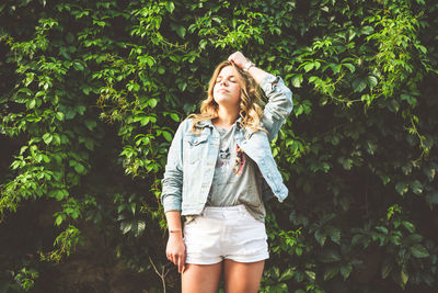 Woman with hand in hair standing against plants