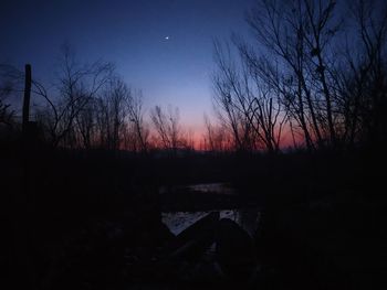 Silhouette bare trees by lake against sky during sunset