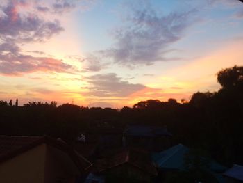 Silhouette trees and houses against sky during sunset