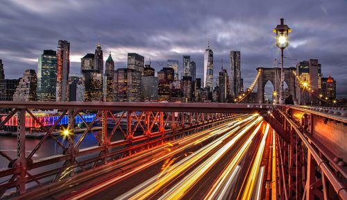 Light trails on city street amidst buildings against sky at dusk