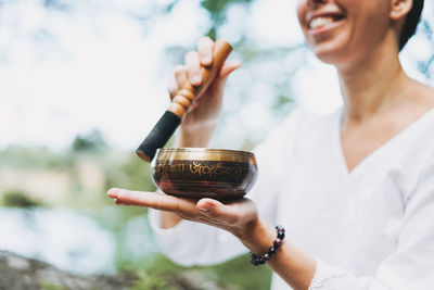 Young smiling woman playing on brass tibetan singing bowl outdoor. sound therapy and meditation