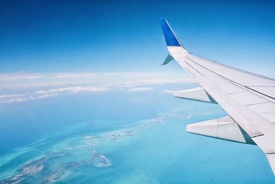 Aerial view of airplane wing over sea against blue sky