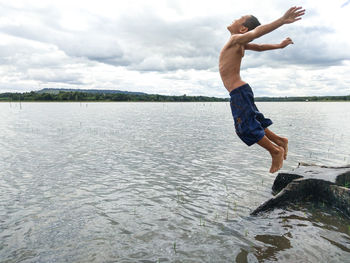 Full length of shirtless man jumping in lake against sky