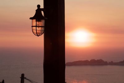 Silhouette street light by sea against sky during sunset