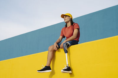 Young man smiling while sitting on wall against clear sky