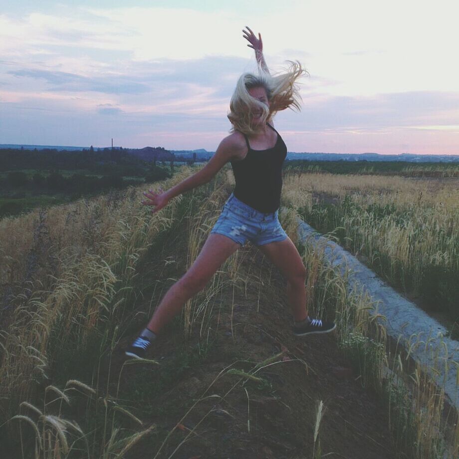 full length, sky, field, leisure activity, casual clothing, young adult, lifestyles, person, landscape, grass, standing, front view, cloud - sky, jumping, nature, tranquility, arms outstretched, young women