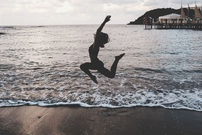 Full length of woman jumping over sea against sky