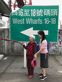 Side view of woman standing with senior person against sign board on street