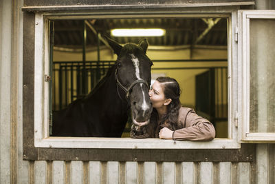 Young woman kissing horse in stable