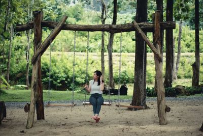 Full length of young woman swinging in forest