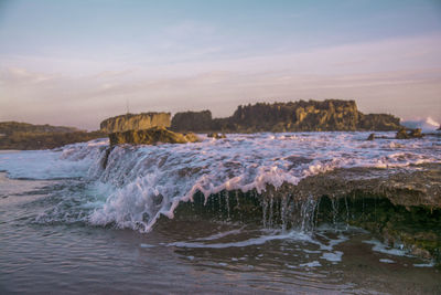 Waves splashing on rocks at shore against sky