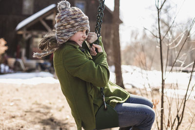 Cheerful girl swinging at playground during winter