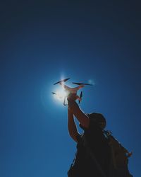 Low angle view of man holding quadcopter against clear blue sky