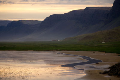 Scenic view of river by mountains against sky during sunset