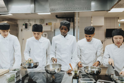 Male and female trainees with saucepans preparing food in culinary school