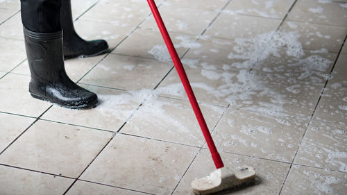 Low section of person wearing rubber boots while washing tiled floor
