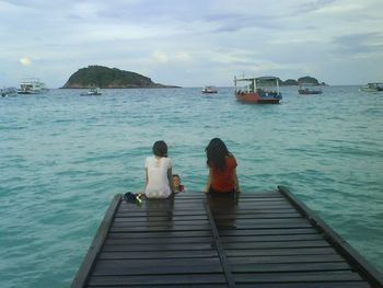 Rear view of people sitting on sea against sky