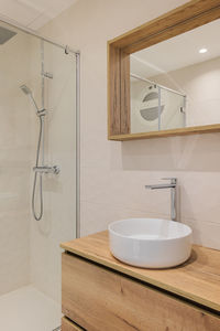 Modern bathroom with shower, round white sink, wooden base and mirror frame. 