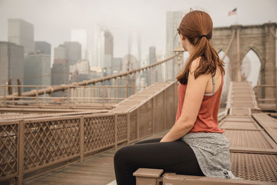 Woman sitting on bridge against sky