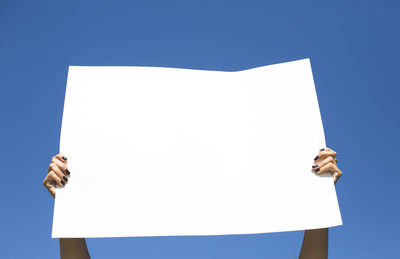 Low angle view of woman holding placard against blue sky