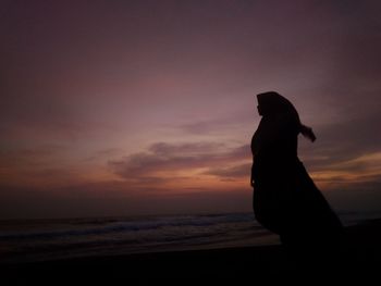 Silhouette woman standing on beach against sky during sunset