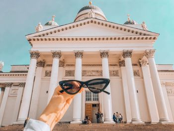 Cropped hand of woman holding sunglasses against cathedral