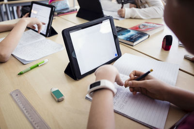 High angle view of students learning through digital tablets in classroom