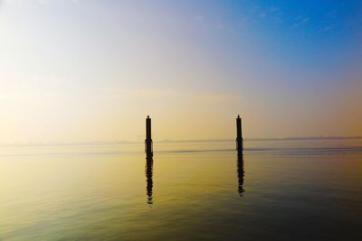 Wooden posts in sea against sky during sunset