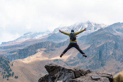 Rear view of man jumping on cliff against landscape