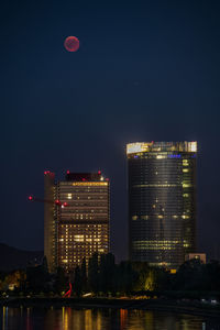 Illuminated buildings by river against sky in city at night