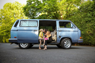 Little girls and mom sitting in doorway of vintage van giving a kiss