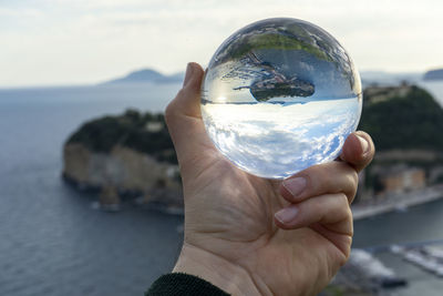 Midsection of person holding crystal ball against sky