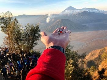 Cropped image of hand holding ring against mountains during foggy weather