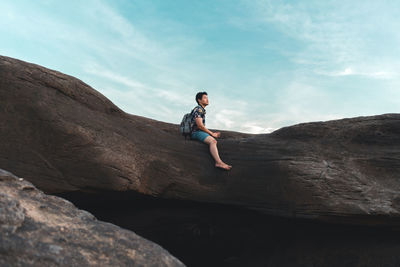 Side view of man on rock against sky