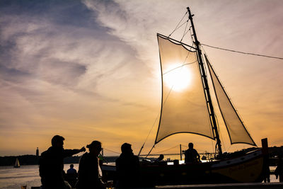 Silhouette people at harbor against cloudy sky during sunset