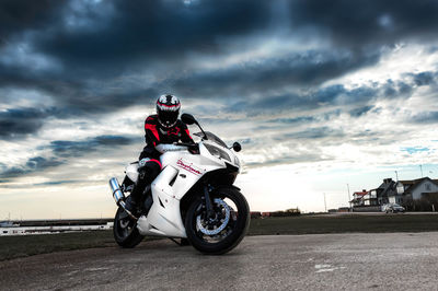 Man riding motorcycle on road against cloudy sky