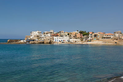 Buildings by sea against clear sky