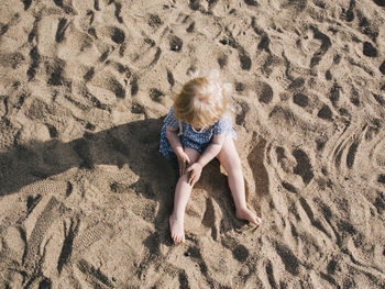 Blond girl sitting on sand barefoot
