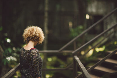 Side view of mid adult woman with curly hair standing by railing