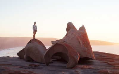 Woman standing on rock at beach against clear sky during sunset