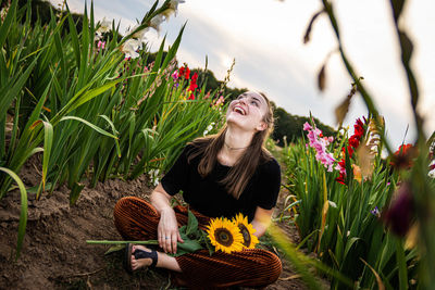 Young woman holding sunflowers while sitting on land