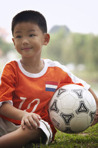 Smiling of boy with soccer ball sitting on field at park