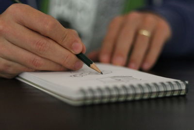 Midsection of woman drawing in notepad on table