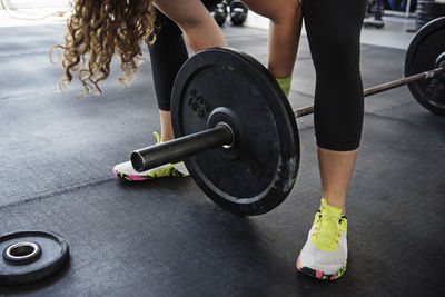 Midsection of woman exercising with barbell at crossfit gym