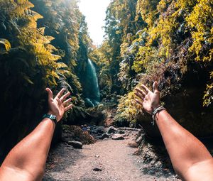 Cropped hands of man reaching waterfall in forest