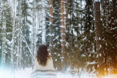 Rear view of woman walking in snow covered forest