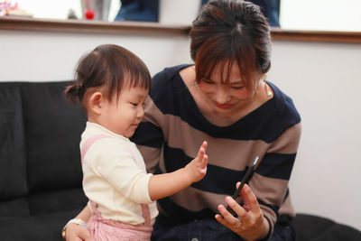 Close-up of mother holding baby and mobile phone at home