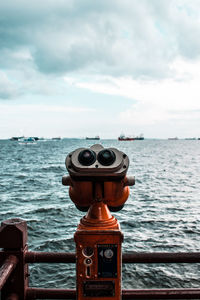 Close-up of coin-operated binoculars by sea against sky