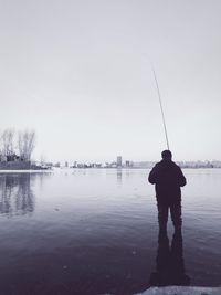 Rear view of man fishing in lake against sky